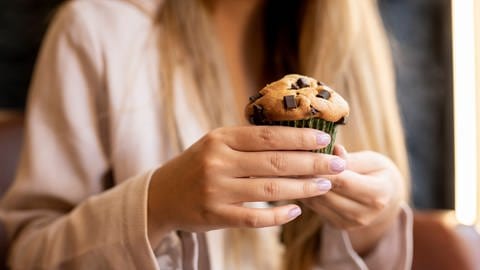 Einsamkeit könnte das Essverhalten verändern: Das Verlangen nach süßem Essen wird höher | Eine Frau hält einen Muffin. (Foto: IMAGO, IMAGO / Westend61)